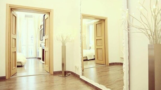 A hallway with wooden flooring, a mirror reflecting the room, and a white vase with branches. - Relais Sistina (Rome)