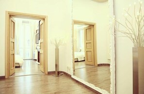 A hallway with wooden flooring, a mirror reflecting the room, and a white vase with branches. - Relais Sistina (Rome)