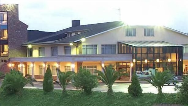 Un hotel moderno con fachada de vidrio, techo plano y jardín cuidado.