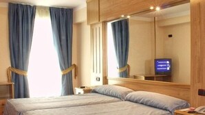 Habitación de hotel con una cama grande, un armario de madera, un escritorio con silla, un televisor y una alfombra roja a cuadros.
