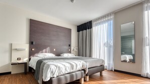 A modern hotel room with a large bed, wooden flooring, a nightstand, a bedside table, and a large mirror. - Le Merceny Motel (Bastogne)
