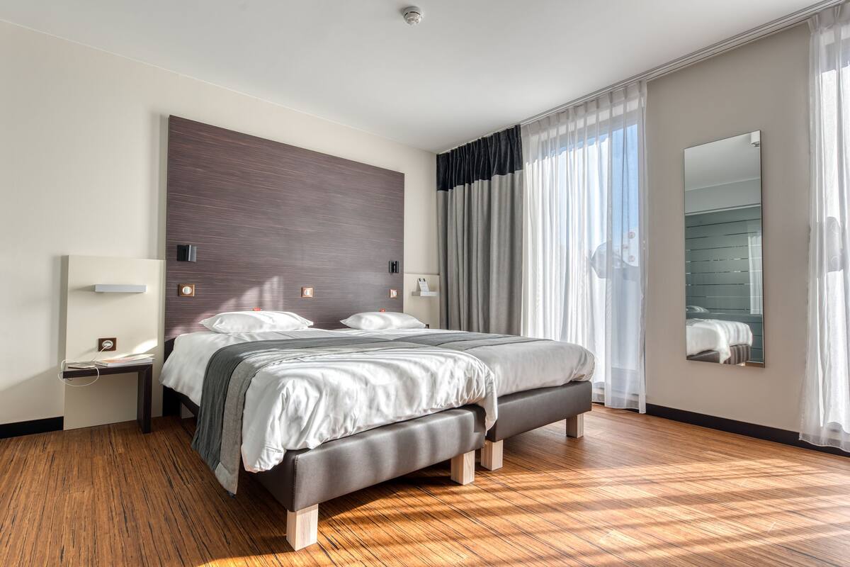 Ein modernes Hotelzimmer mit einem großen Bett, Holzboden, einem Nachttisch und einem großen Spiegel.