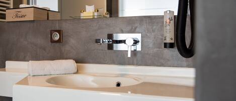 A modern bathroom with a large sink, a handheld showerhead, and a tissue box on the counter.