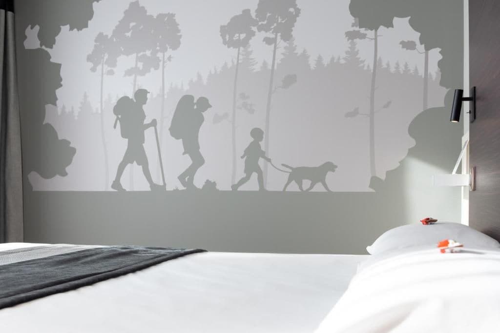 A bedroom with a bed, a wall-mounted light, and a silhouette mural of a family hiking.