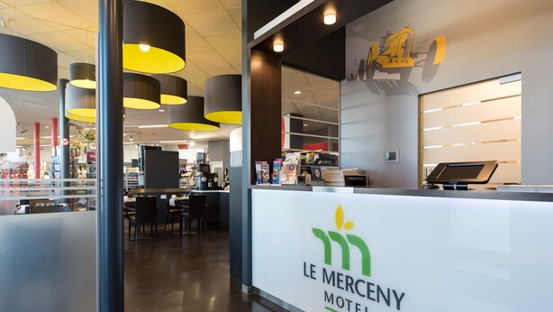 A modern interior of Le Merceney Motel with a reception desk, seating area, and a visible restaurant section. - Le Merceny Motel (Bastogne)