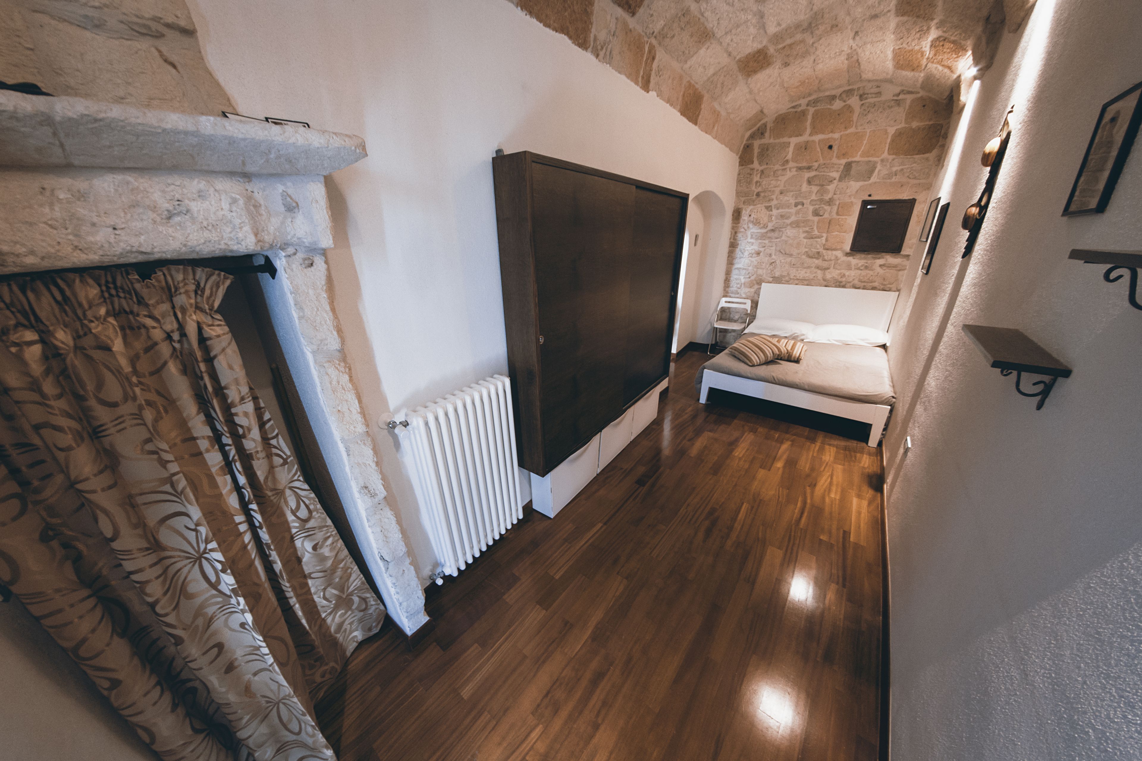 Ein Zimmer mit Steinwand, Holzboden, einem Bett, einem Heizkörper und einem großen Schrank.