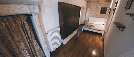 Une pièce avec un mur en pierre, un plancher en bois, un lit, un radiateur et une grande armoire.