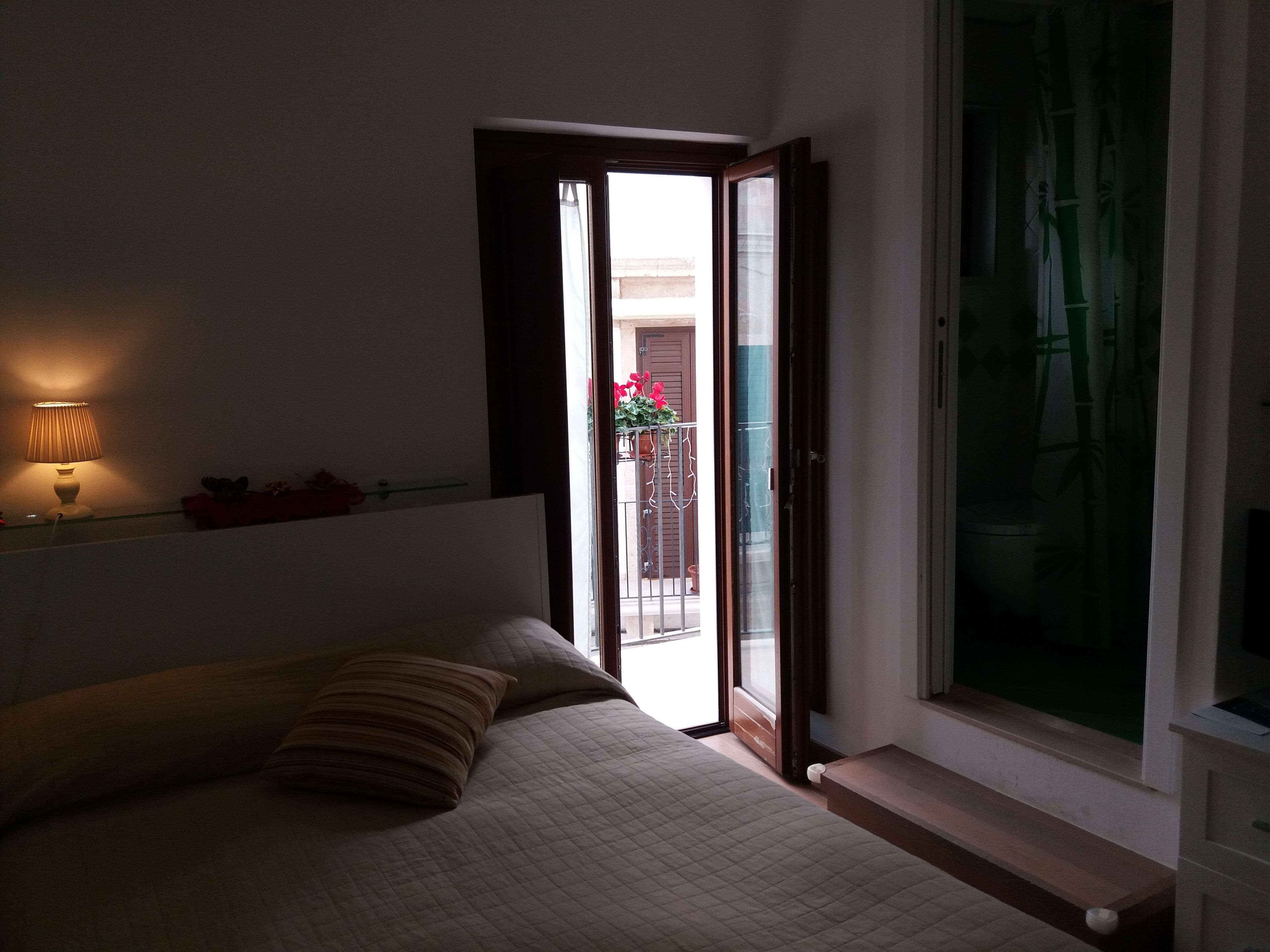 Une chambre à coucher avec un lit, une lampe de chevet, une fenêtre et une vue sur le balcon extérieur.