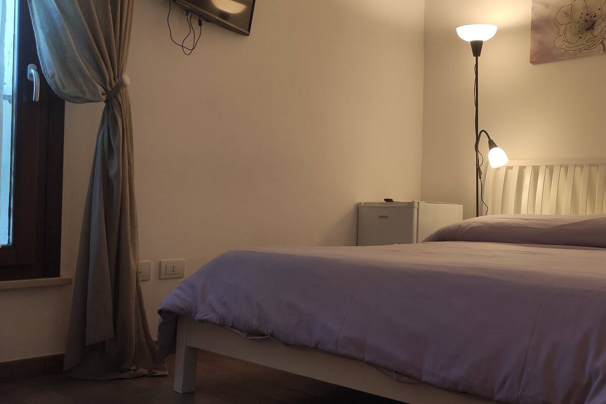 A bedroom with a bed, a bedside table, a lamp, and a window with curtains.