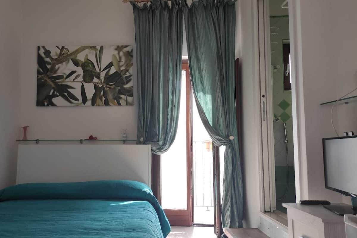 A bedroom with a bed, a TV, a window with curtains, and a painting on the wall.