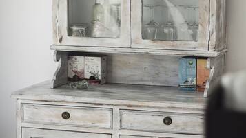 Un aparador blanco de madera envejecida con puertas de cristal, que contiene copas y cajas.