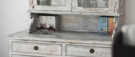 Un aparador blanco de madera envejecida con puertas de cristal, que contiene copas y cajas.