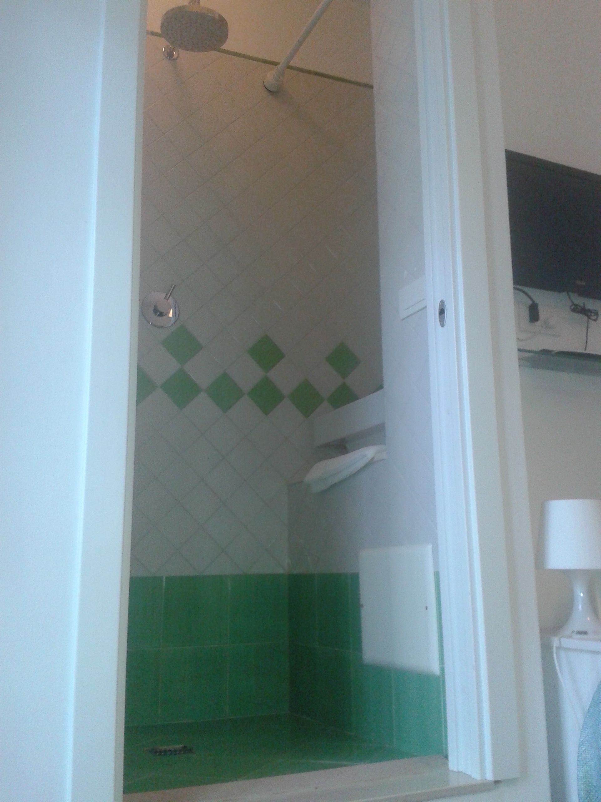 A bathroom with a shower, green and white tiled walls, a white towel hanging, and a white ceiling fan.