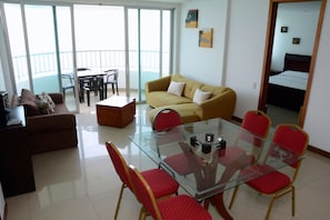 Een moderne woonkamer met een glazen eettafel, rode stoelen, een bank en een balkon met een tafel en stoelen.