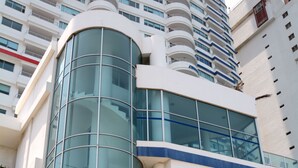 A modern building with a curved glass facade, a prominent entrance with steps, and a logo on the wall. - Apartmentos Playa Palmetto (Cartagena)