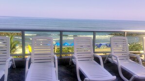 A balcony with white lounge chairs facing a beach with blue umbrellas. - Apartmentos Playa Palmetto (Cartagena)