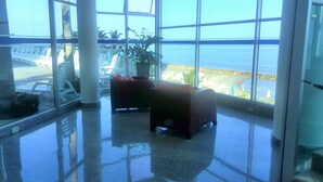 A spacious lobby with a large glass wall offering a view of the beach. There are several lounge chairs and a potted plant. - Apartmentos Playa Palmetto (Cartagena)