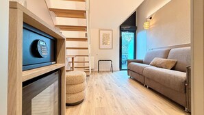 A modern living room with a sofa, a small round rug, a wooden staircase, and a wall-mounted TV.