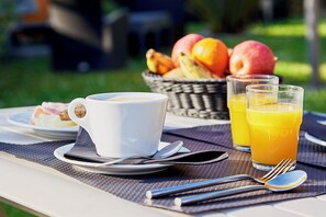 A breakfast setting with a cup of coffee, a glass of orange juice, and a basket of fruits on a table.