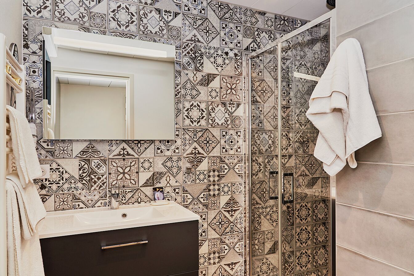 Casa de banho com azulejos estampados, uma pia branca, um armário escuro e uma toalha pendurada na parede.