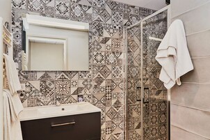 Casa de banho com azulejos estampados, uma pia branca, um armário escuro e uma toalha pendurada na parede.