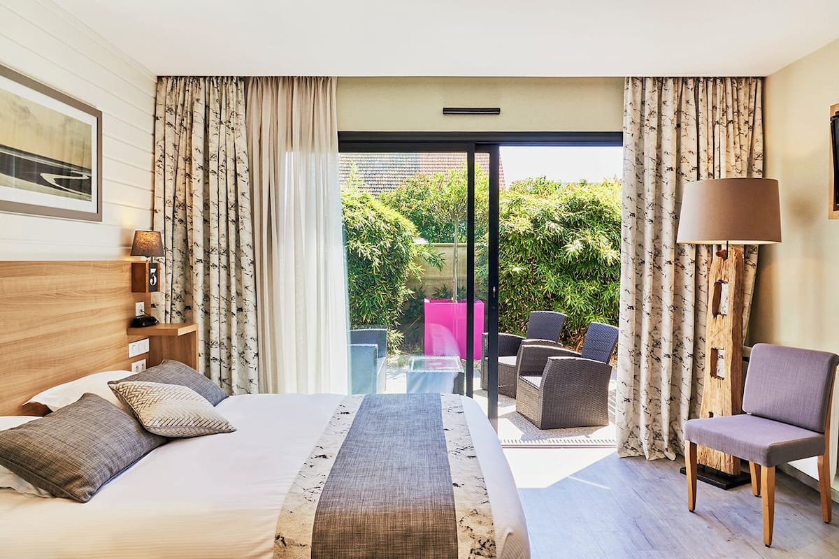 A hotel room with a bed, a chair, a table, and a view of the outdoors.