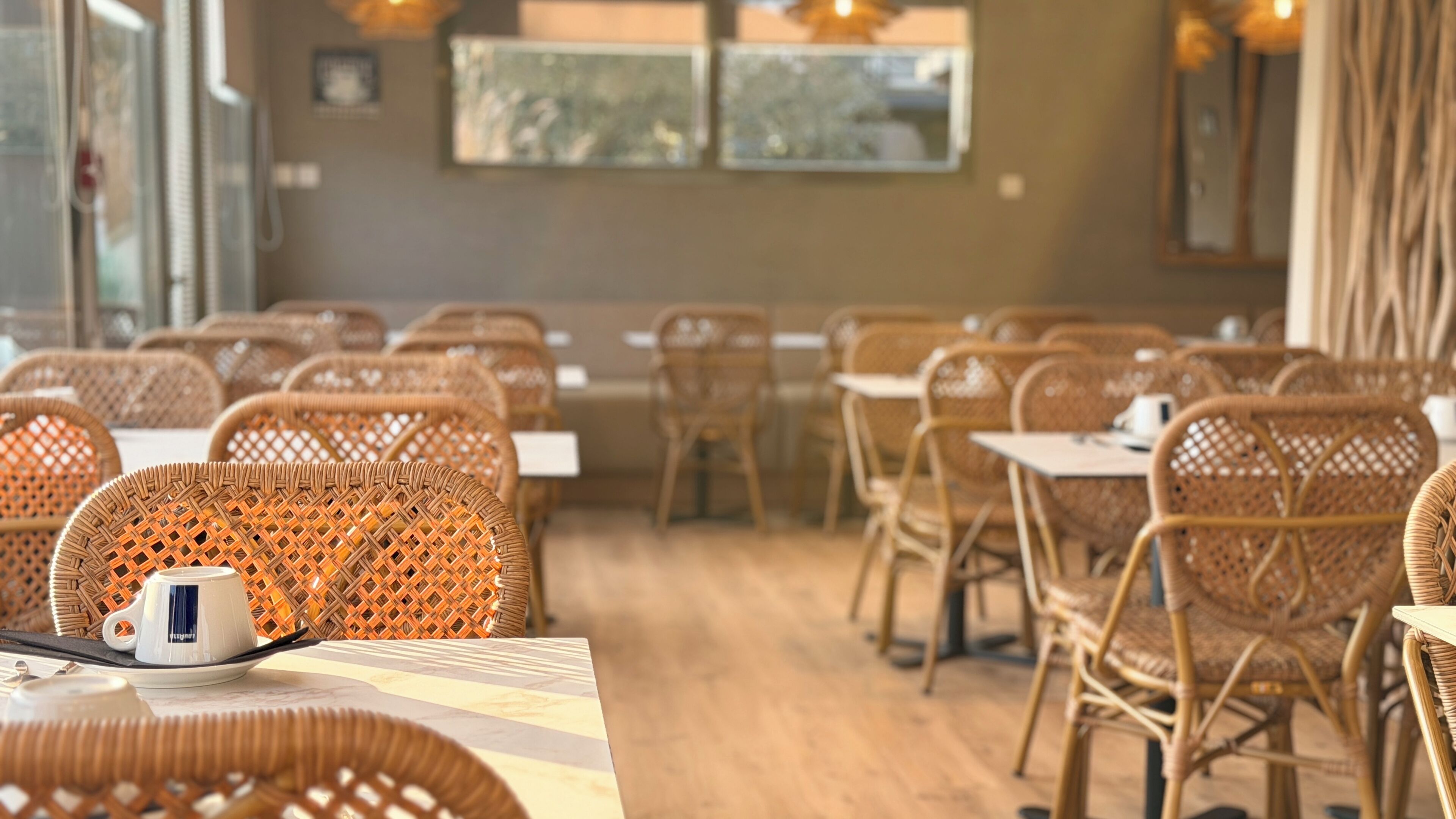 L’intérieur d’un restaurant, avec des chaises et des tables en osier, un appareil à café et des œuvres d’art accrochées aux murs.