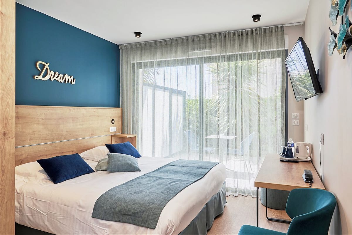A hotel room with a bed, a desk, a television, and a large window with curtains.