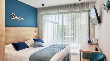 A hotel room with a bed, a desk, a television, and a large window with curtains.