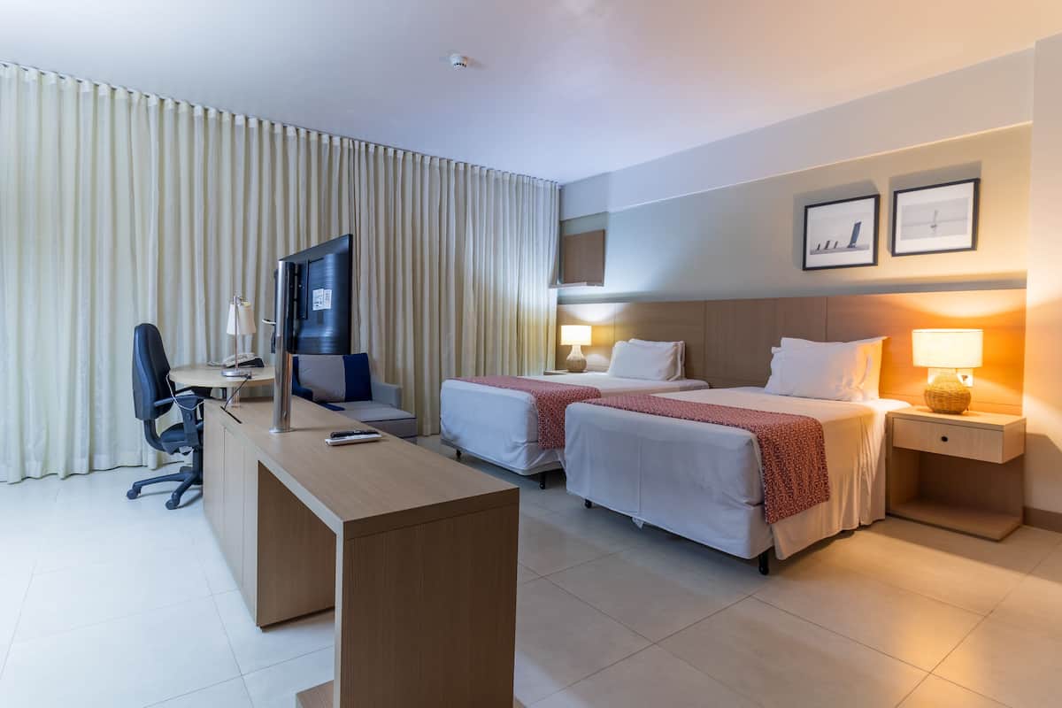 A hotel room with a desk, two beds, a TV, and a lamp.