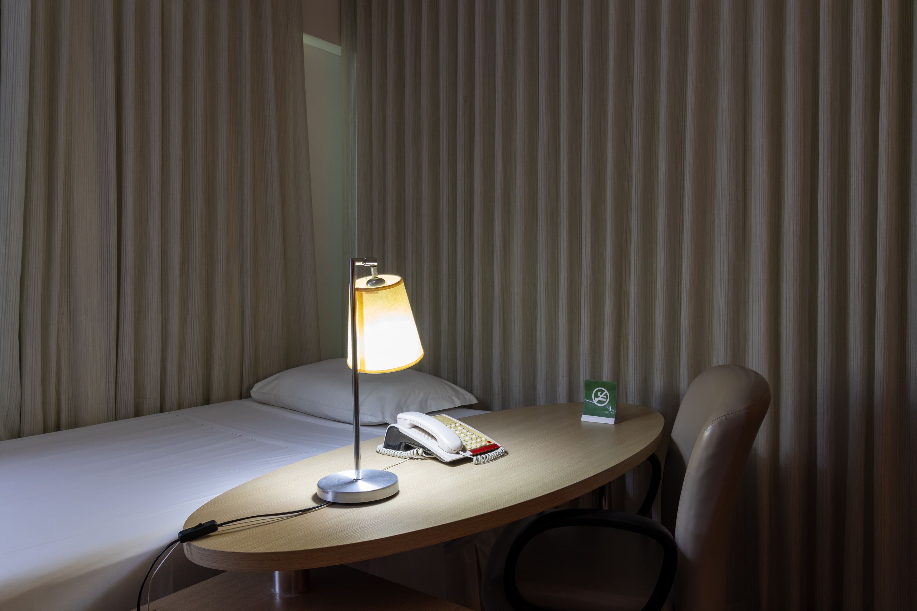 Una habitación de hotel con una cama, un escritorio con lámpara, un teléfono y una silla.