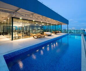 Un edificio moderno con fachada de vidrio, piscina en la azotea y vistas al horizonte de la ciudad.