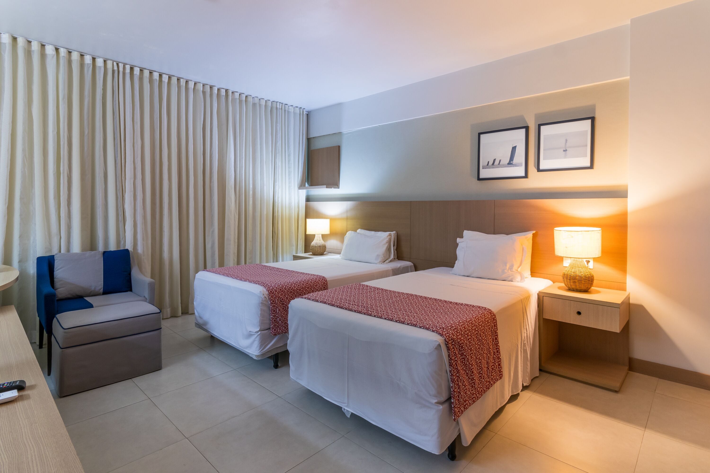 Una habitación de hotel con dos camas, un escritorio, una silla y una mesita de noche con una lámpara.
