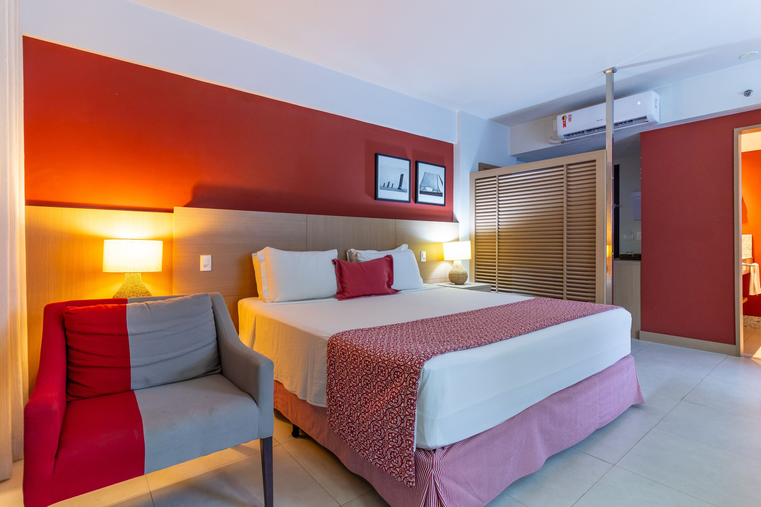 Quarto de hotel com cama, sofá, abajur e ar condicionado fixado na parede.