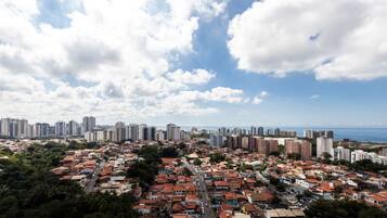 A cityscape with a mix of high-rise buildings and low-rise residential areas, a clear sky, and a distant view of the sea.