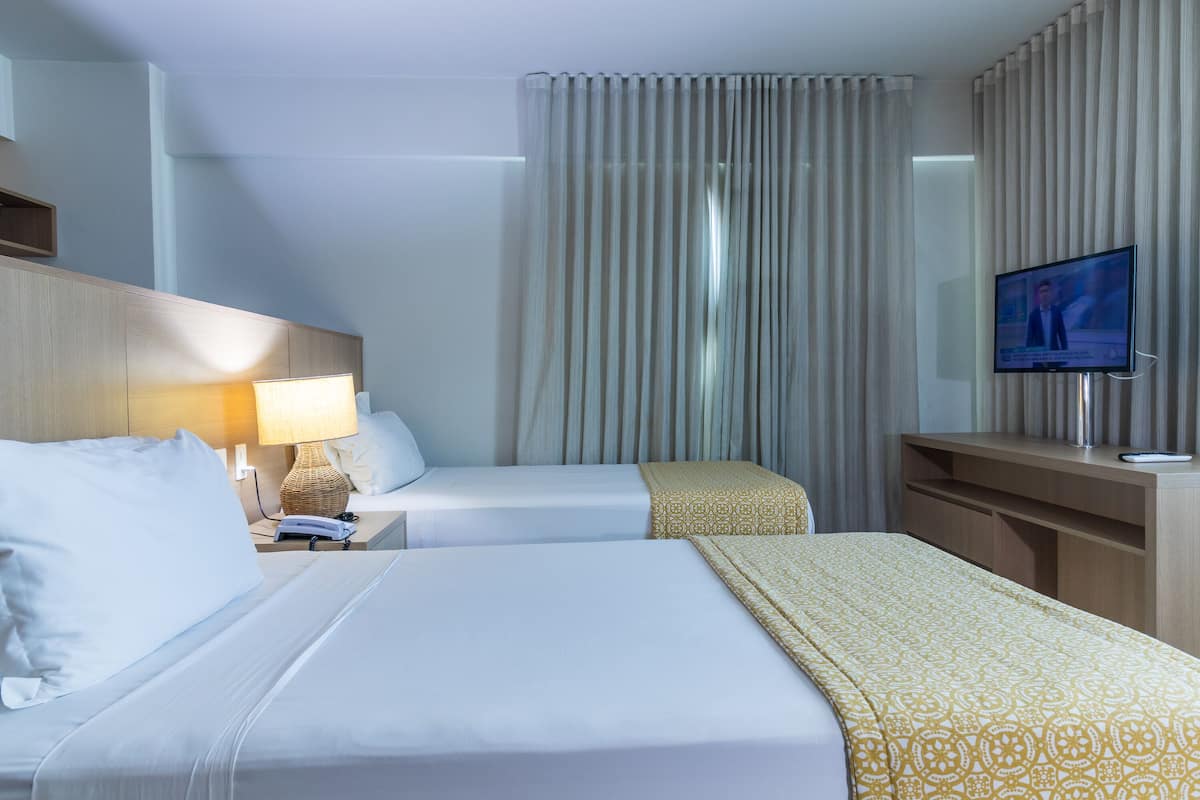 A hotel room with two beds, a TV, a desk, and a window with curtains.