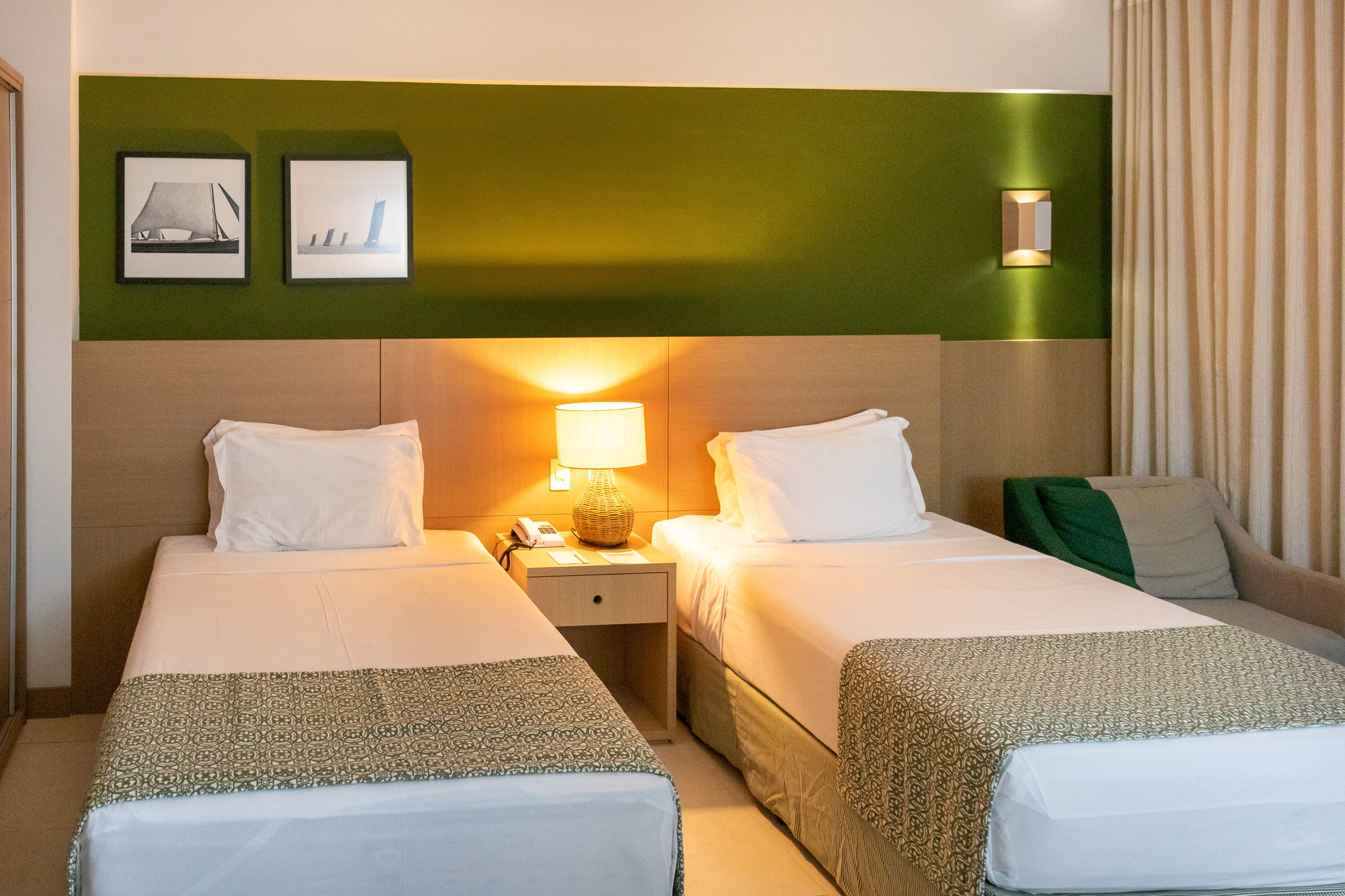 Una camera d'albergo con due letti, un comodino con una lampada e una luce a parete.