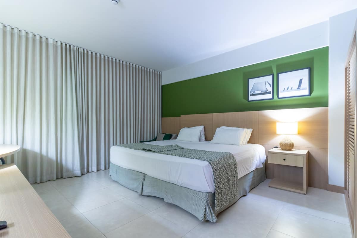A modern hotel room with a large bed, a bedside table with a lamp, and a green accent wall.