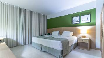 A modern hotel room with a large bed, a bedside table with a lamp, and a green accent wall.