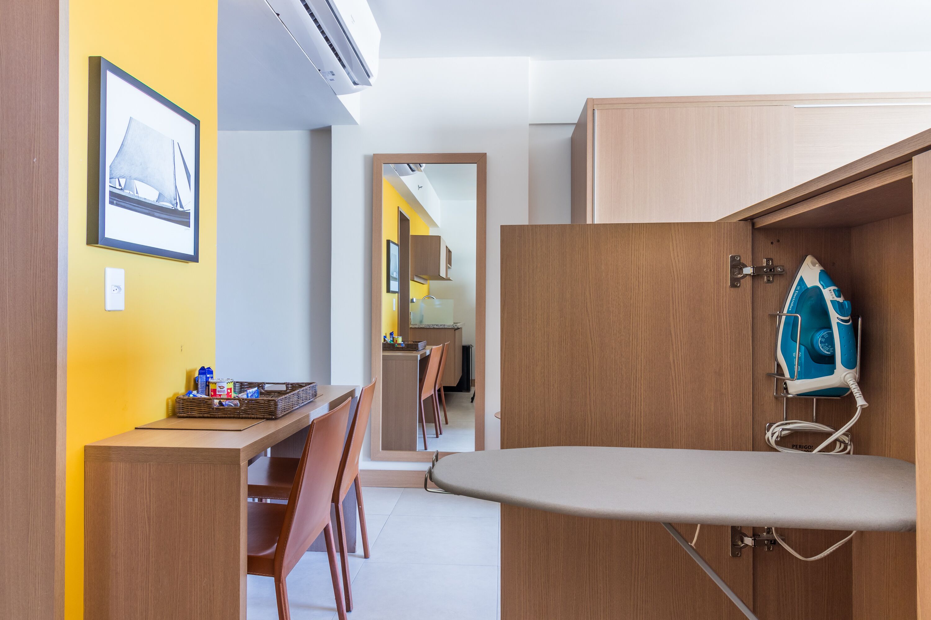 A compact kitchen with wooden cabinets, a dining area with chairs, and a visible ironing board.