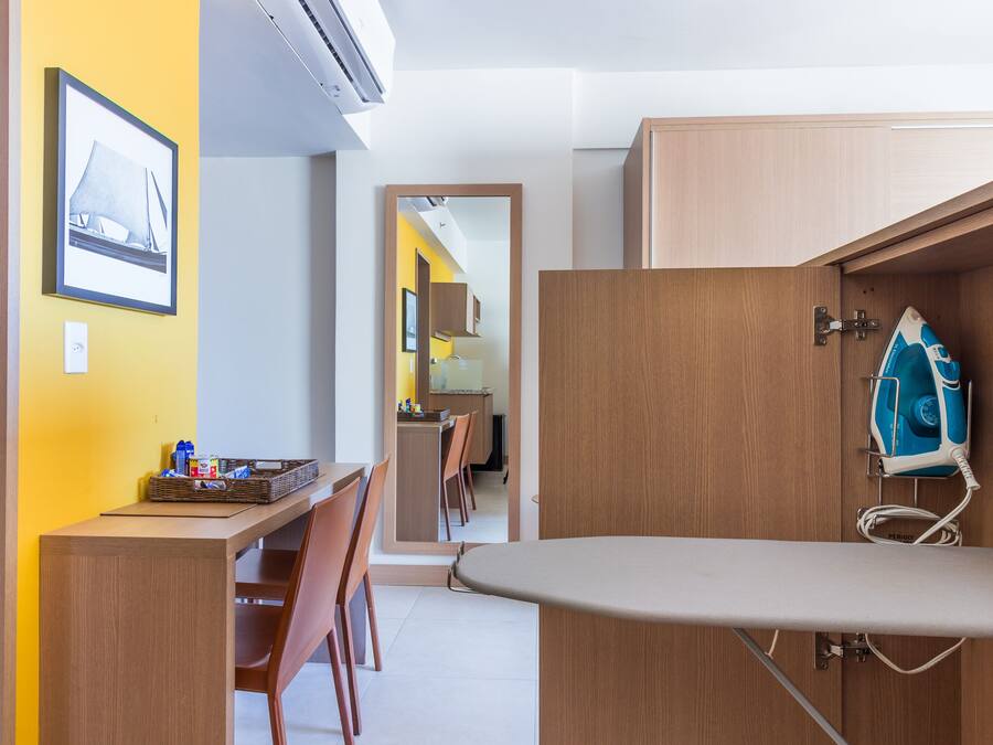 A compact kitchen with wooden cabinets, a dining area with chairs, and a visible ironing board.