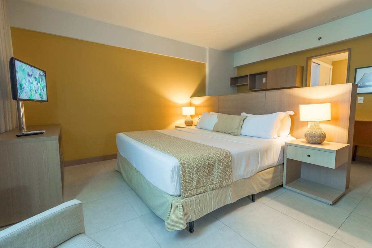 A hotel room with a bed, bedside tables, a TV, and a mirror.