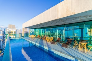 Ein Pool auf dem Dach mit Glaswänden, Liegestühlen und Blick auf die Stadt.