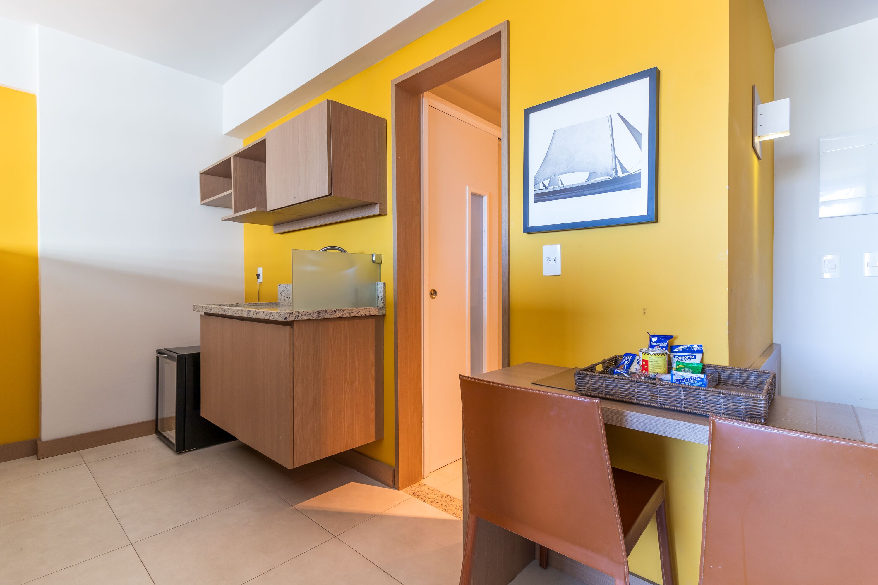 A compact kitchen with a dining area, a small trash bin, and a framed picture on the wall.