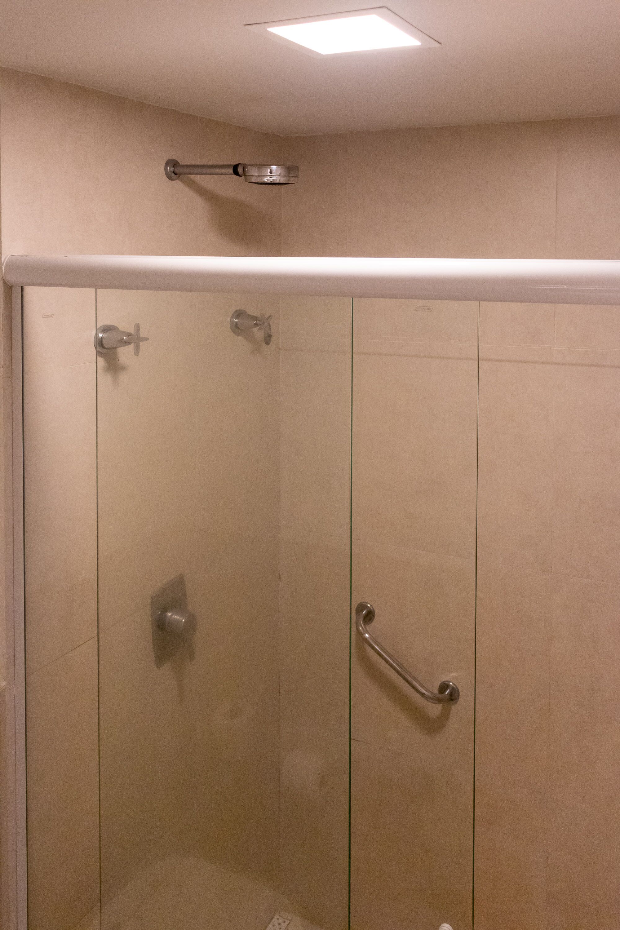 Una ducha sin borde con barra de apoyo, luz de techo y pared con azulejos.