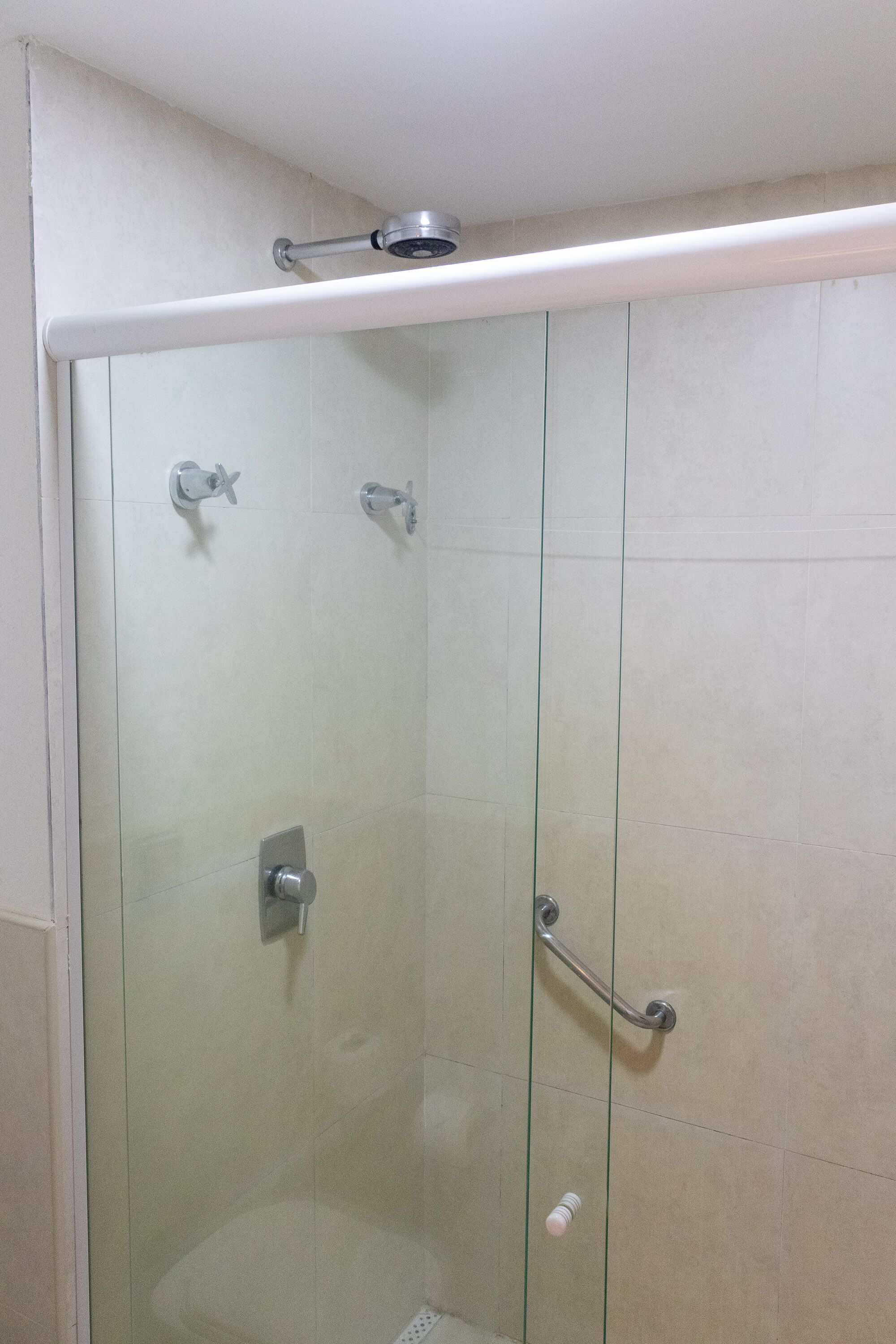 A glass-enclosed shower stall with a handheld showerhead, a handheld showerhead, and a glass door.