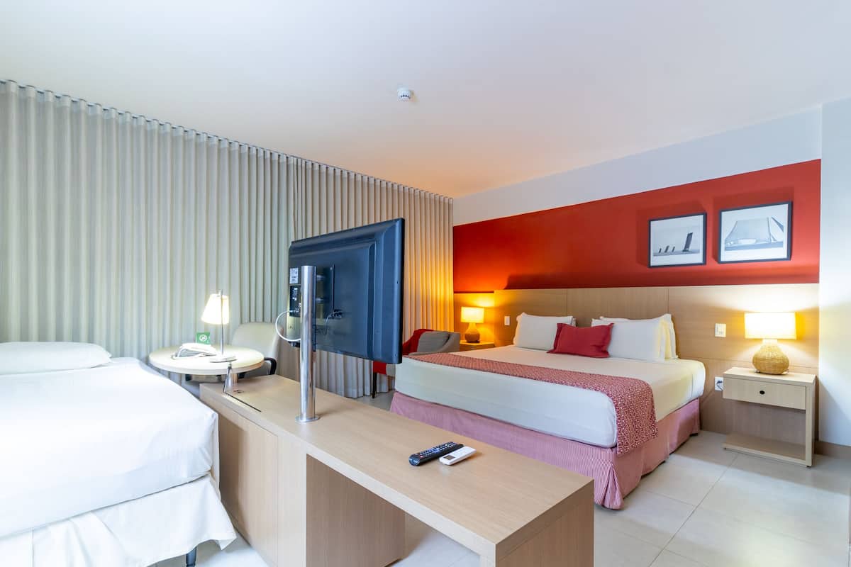 A hotel room with a bed, bedside tables, a desk, a TV, and a door.