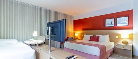 A hotel room with a bed, bedside tables, a desk, a TV, and a door.