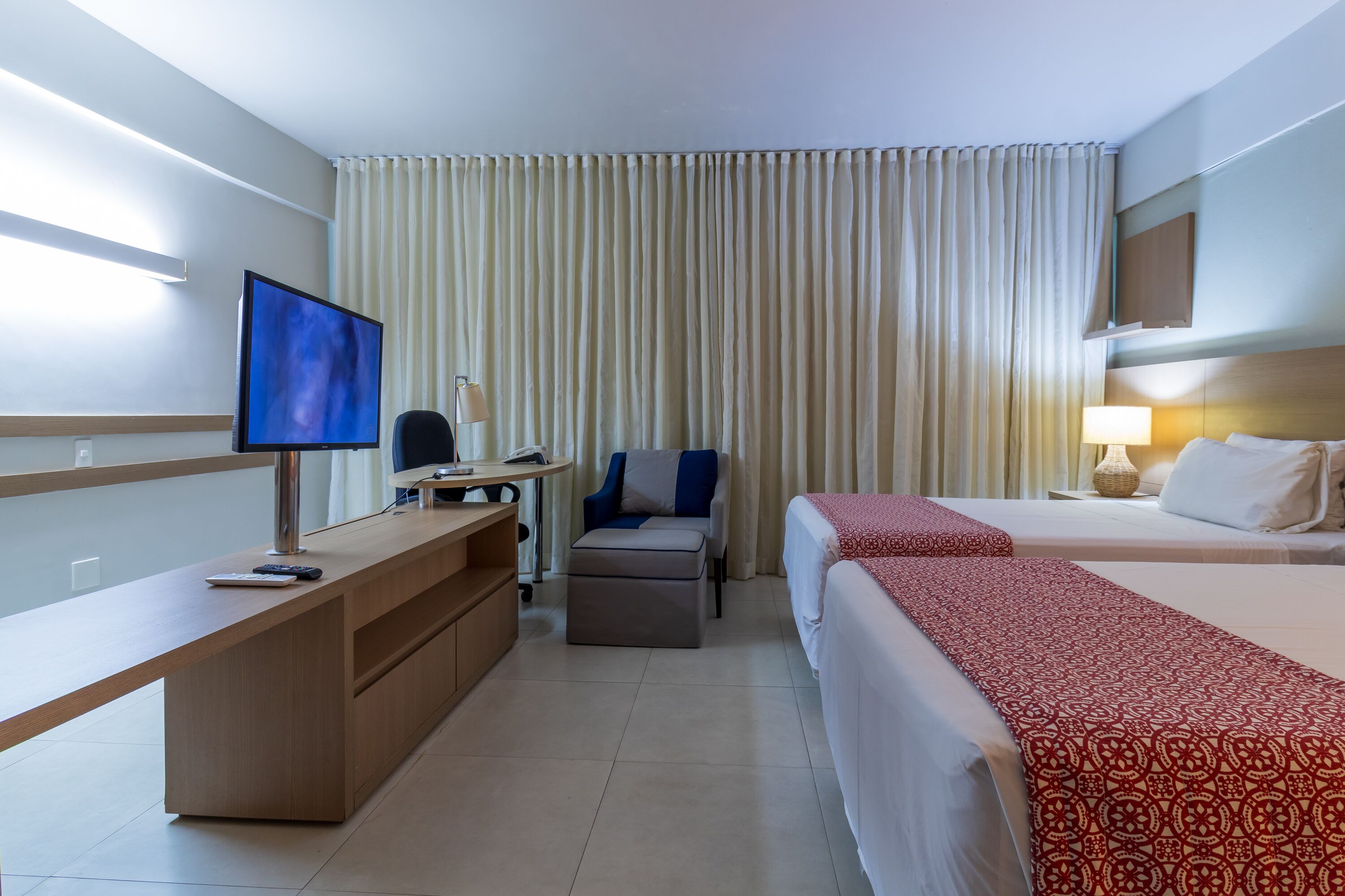 A hotel room with a desk, a chair, a bed, and a TV.