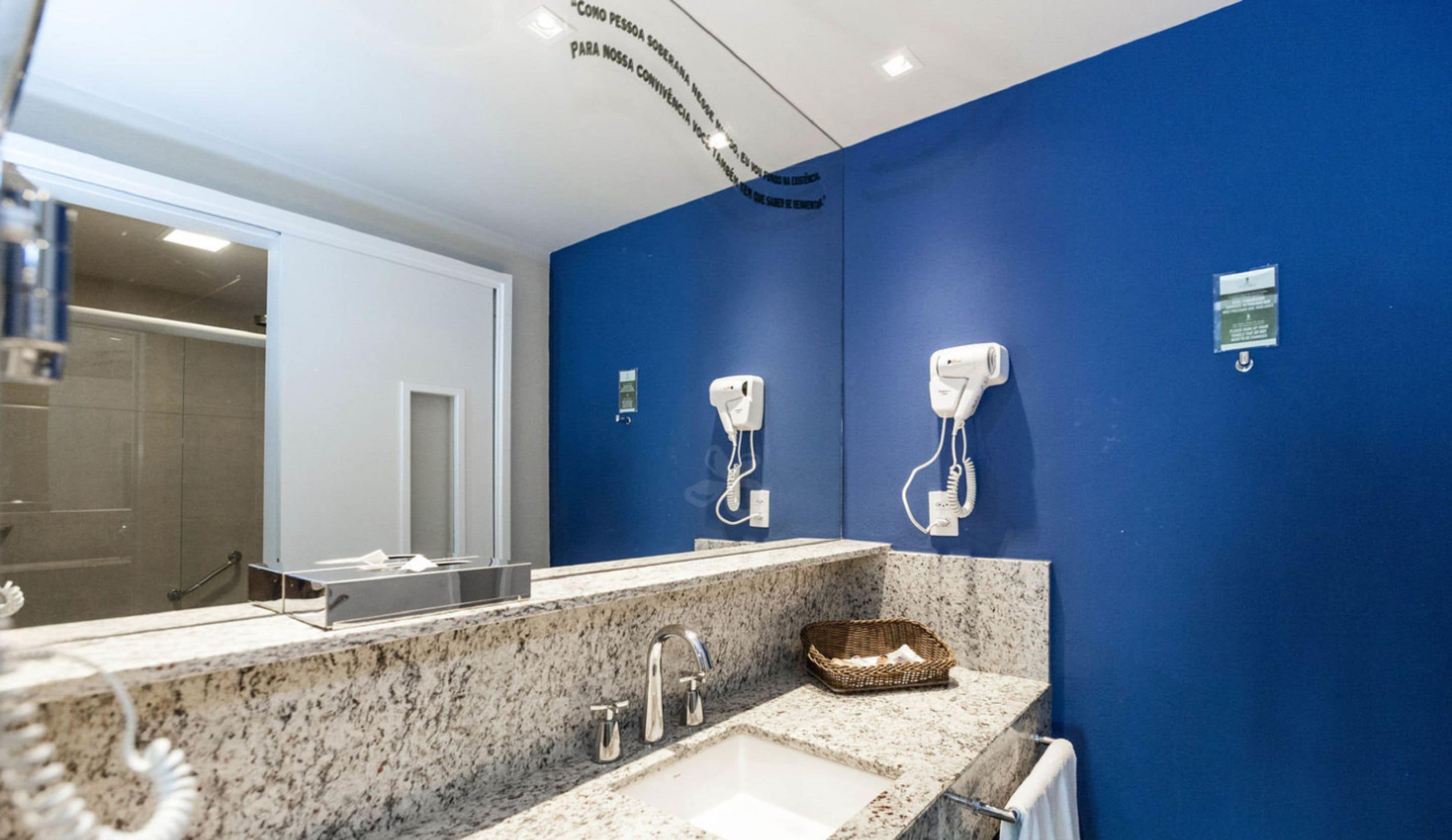 Un baño con pared azul, un lavamanos con encimera de granito y dos secadores de pelo fijados a la pared.